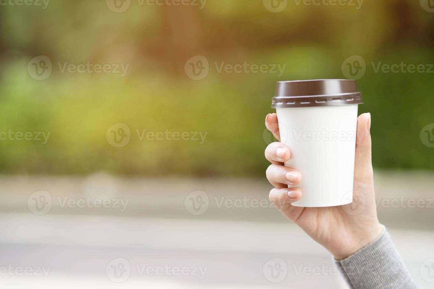 barista en tablier tient dans les mains un cappuccino chaud dans une tasse de papier à emporter blanche. café à emporter au café photo
