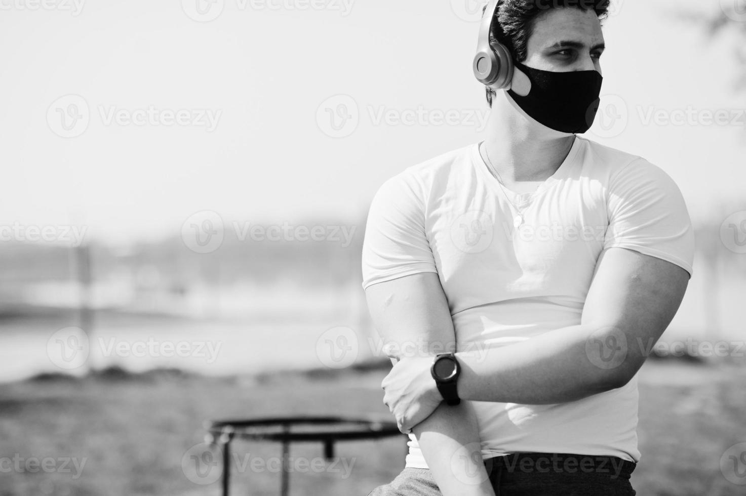 portrait sport arabe homme en masque médical noir posé à l'extérieur avec des écouteurs pendant la quarantaine du coronavirus. photo