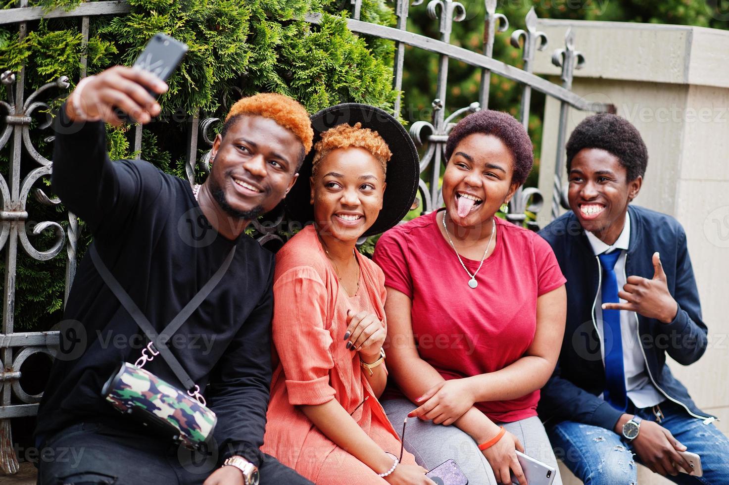 quatre amis africains s'amusant à l'extérieur. deux filles noires avec des gars avec des téléphones portables font du selfie. photo