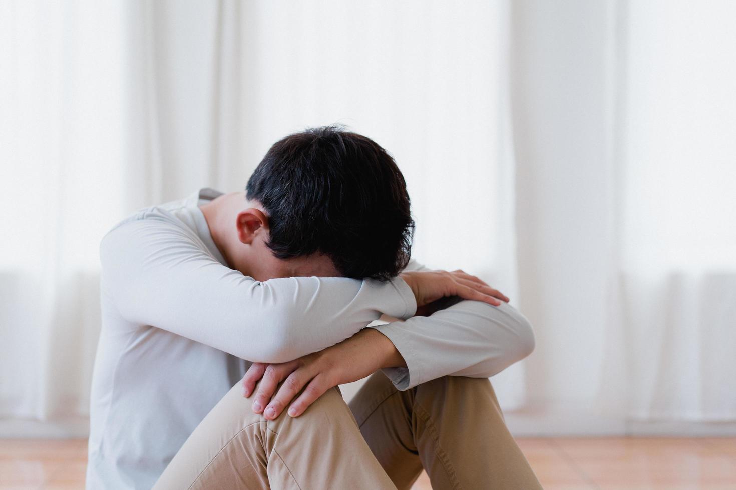 jeune homme asiatique déprimé couvrant le visage par les mains, pleurant seul à la maison, homme bouleversé assis, se sentant malheureux après une querelle ou une rupture, désespoir et solitaire et panique, concept de problème psychologique photo