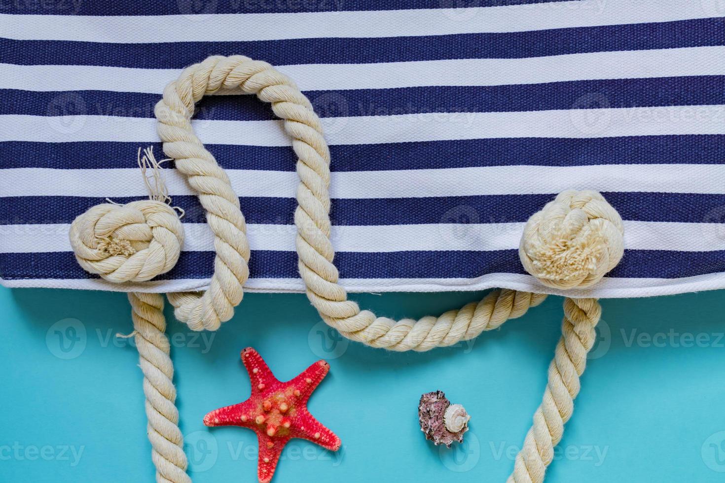 coquillages, étoiles de mer et sac bleu marine à rayures textiles avec nœuds de corde sur fond bleu clair. vacances d'été et concept de vacances photo