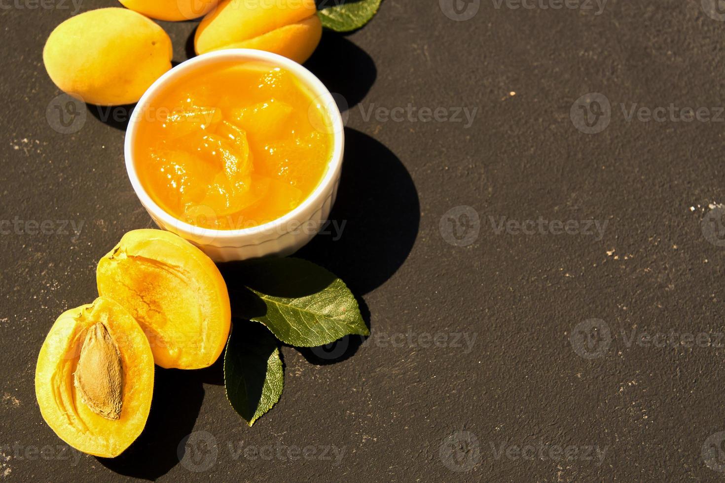 confiture d'abricot biologique maison dans un bol blanc et abricots mûrs sur fond noir. Lumière forte photo