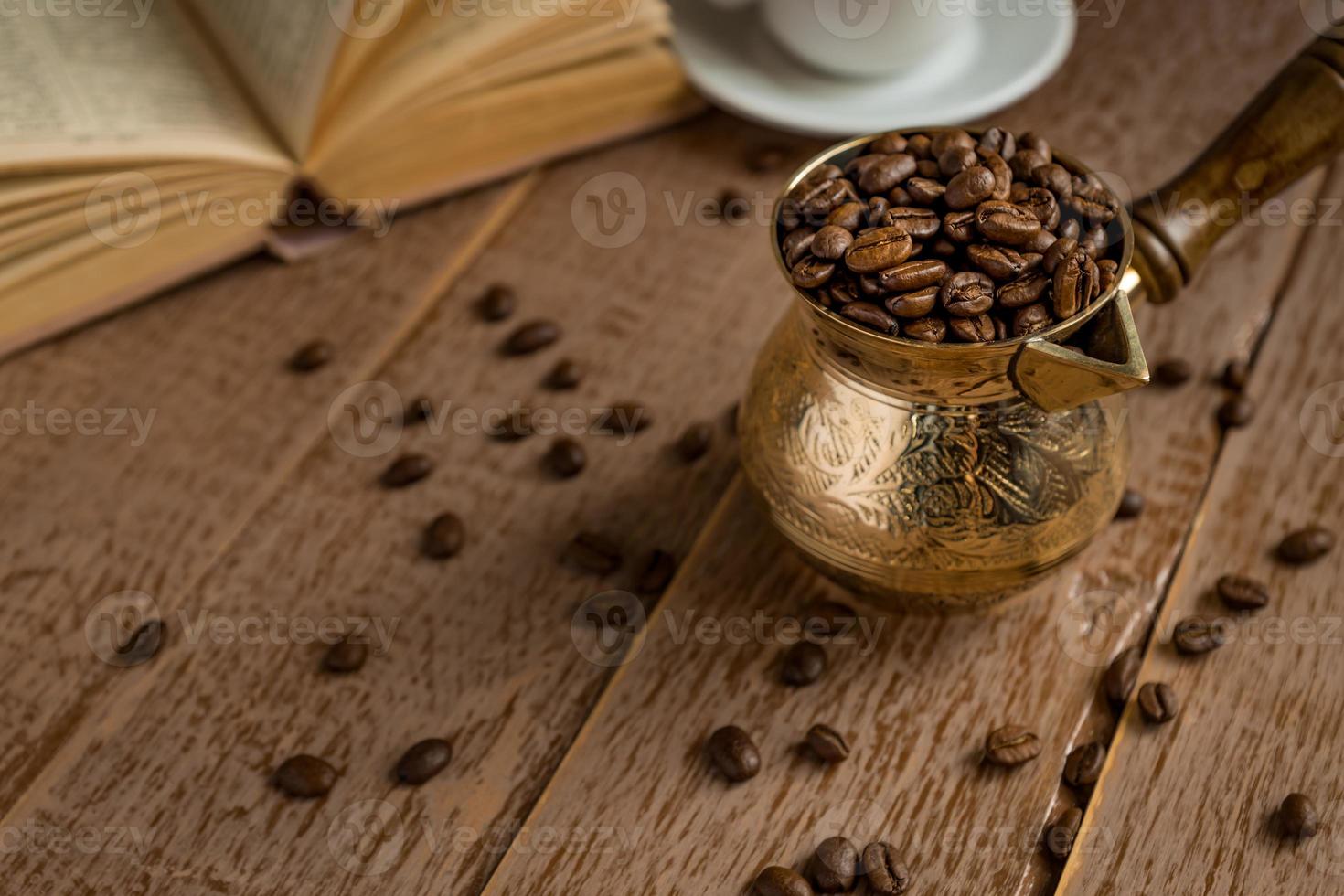 grains de café torréfiés frais dans une cafetière turque traditionnelle cezve livre ouvert et tasse sur une table en bois. photo