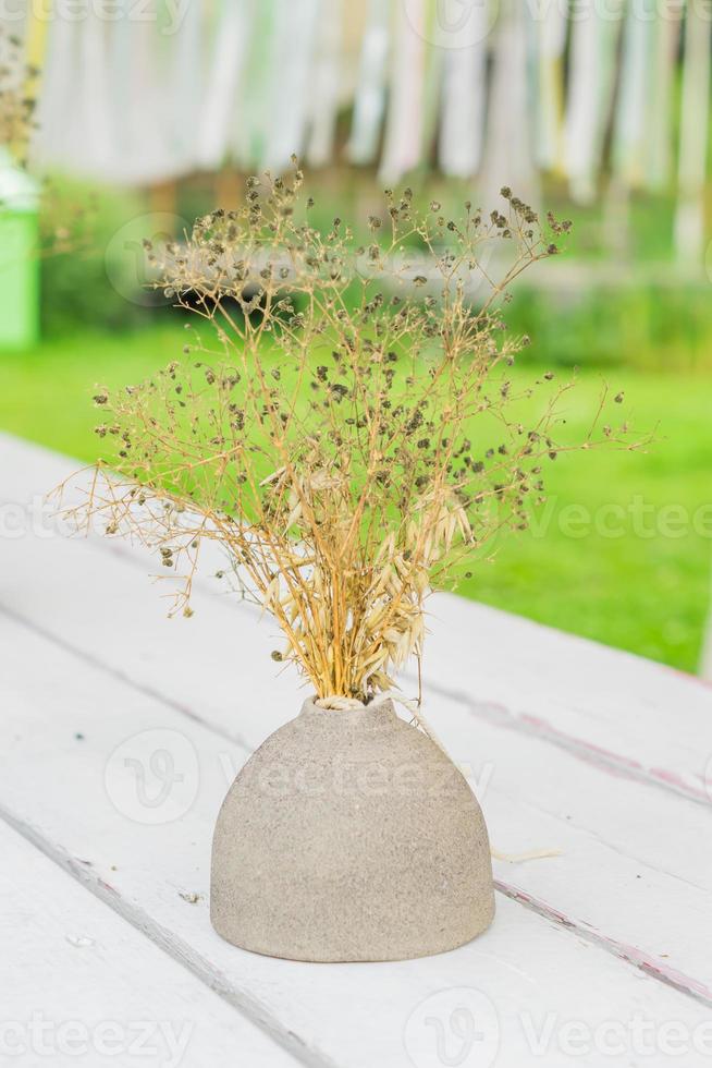 fleurs sèches dans un vase en argile sur une table en bois à l'extérieur photo