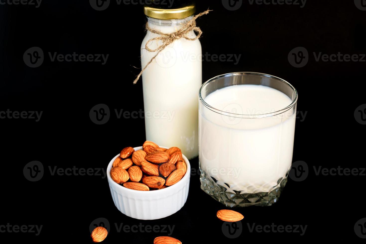 lait d'amande fait maison dans une bouteille et verre avec noix dans un bol en porcelaine blanche sur fond noir. photo