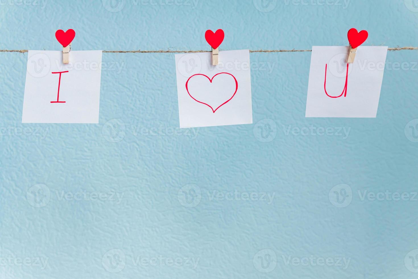 épingles de coeurs d'amour de la saint-valentin rouge accrochées à un cordon naturel sur fond bleu. je t'aime inscription sur des morceaux de papier. photo