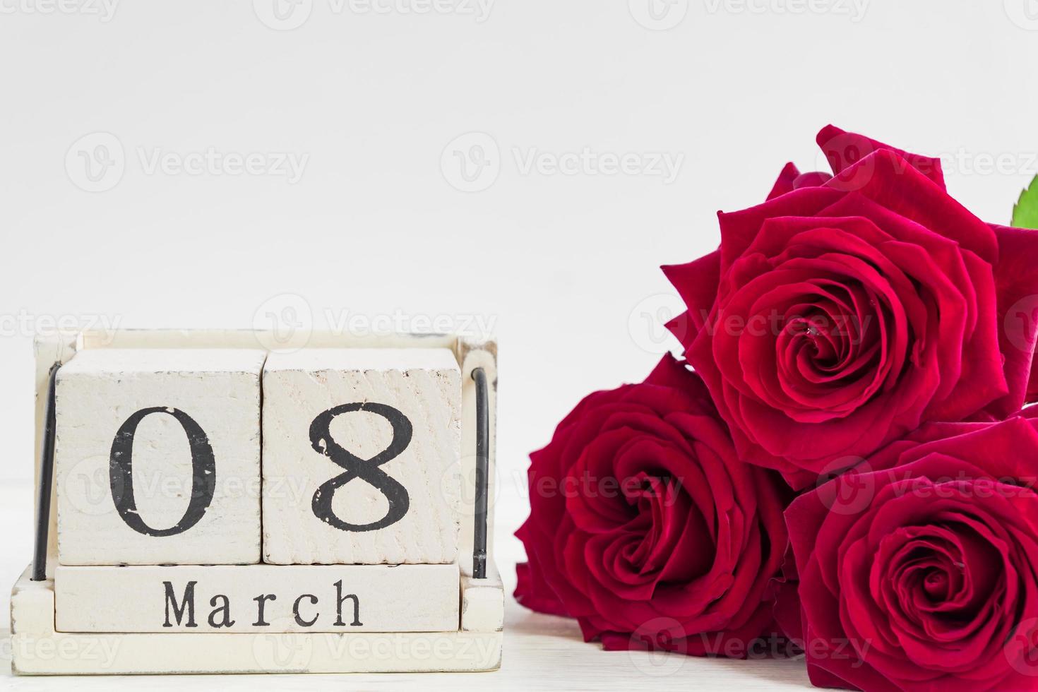 beau bouquet de roses rouges et calendrier de cube en bois sur un fond en bois. le concept de félicitations le 8 mars ou le jour de la femme. photo