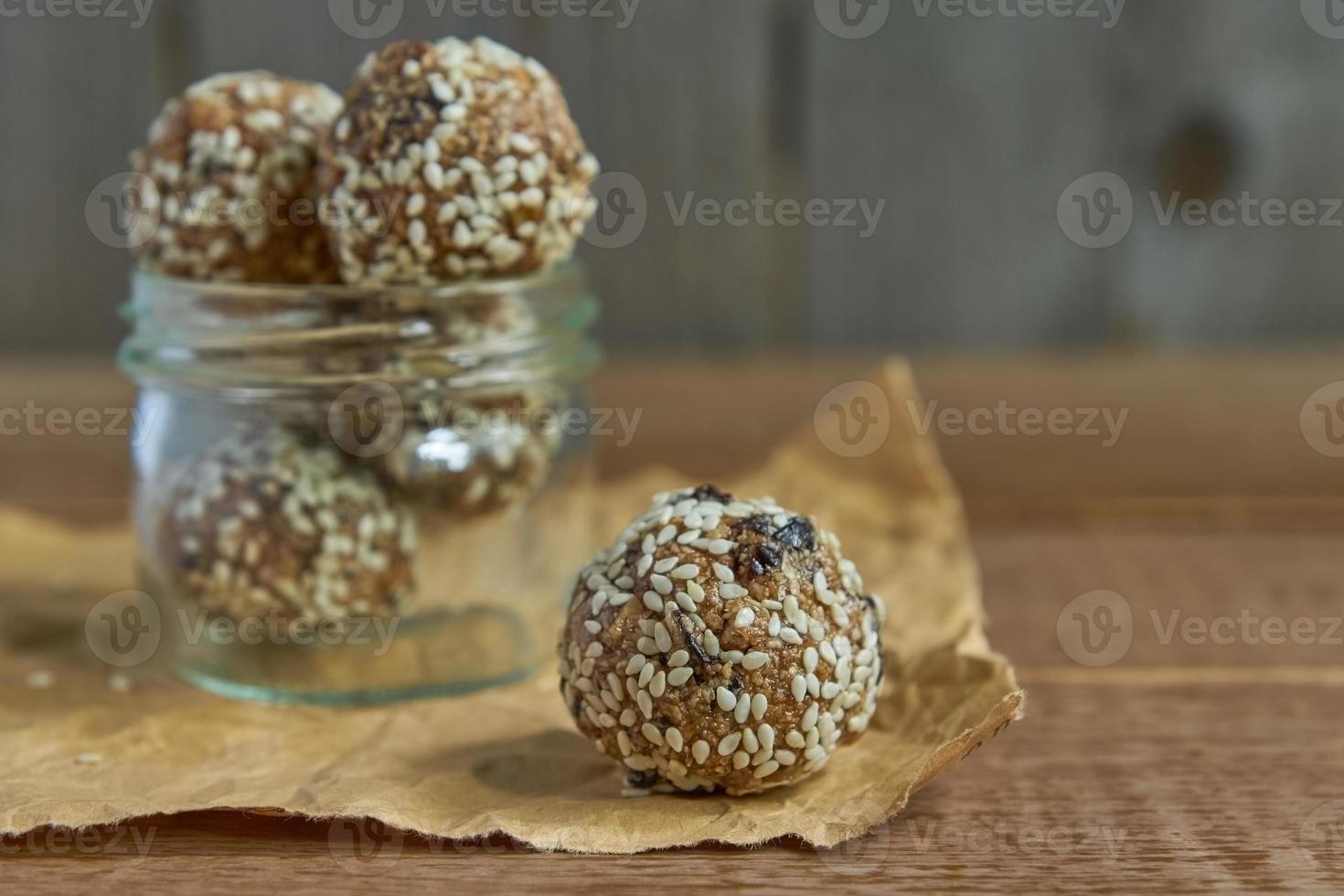 De savoureuses truffes de protéines brutes végétaliennes ou des boules d'énergie avec des pruneaux, des graines et des noix dans un bocal sur fond de bois photo