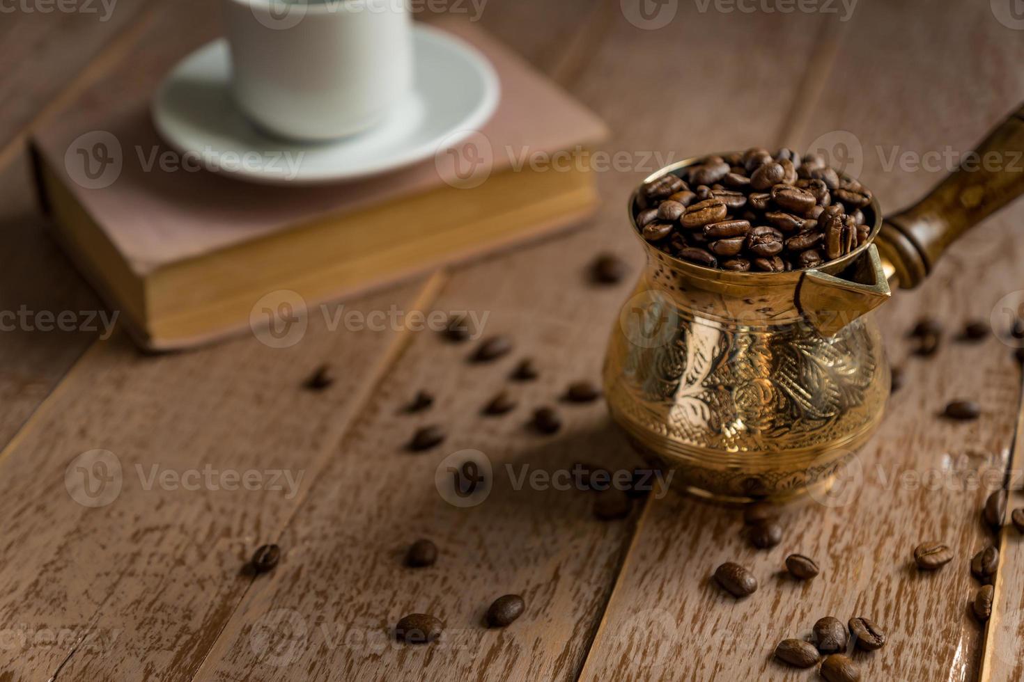 grains de café torréfiés frais dans une cafetière turque traditionnelle cezve livre fermé et tasse sur table en bois. photo