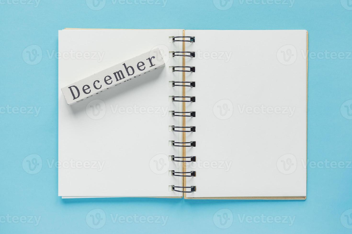 carnet de notes en spirale propre pour les notes et les messages et barre de calendrier en bois de décembre sur fond bleu. mise à plat d'affaires minimale photo