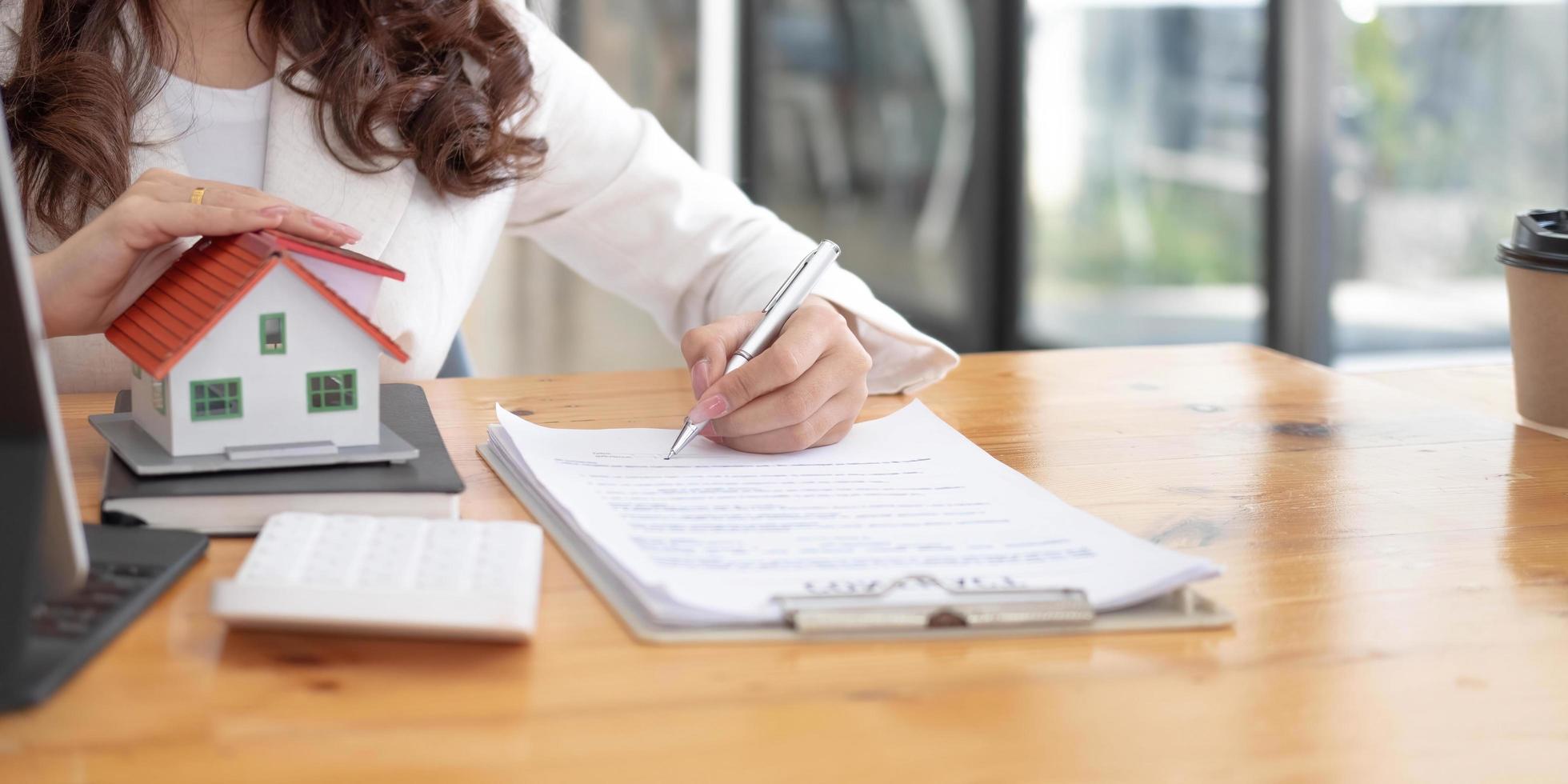 gros plan sur des mains de femme tenant un modèle de maison, des contrats de courtage immobilier à vendre et à louer avec des concepts de prêt hypothécaire d'assurance. photo