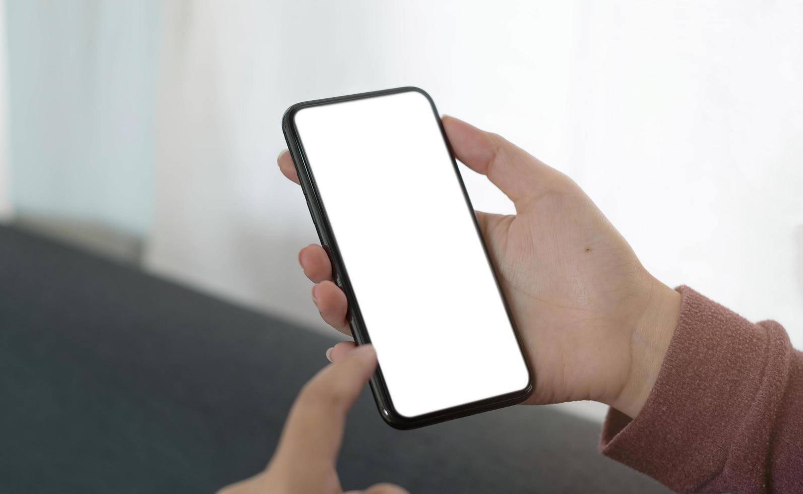 image de maquette téléphone portable à écran blanc vierge. main de femme tenant des SMS à l'aide d'un téléphone portable sur un canapé photo