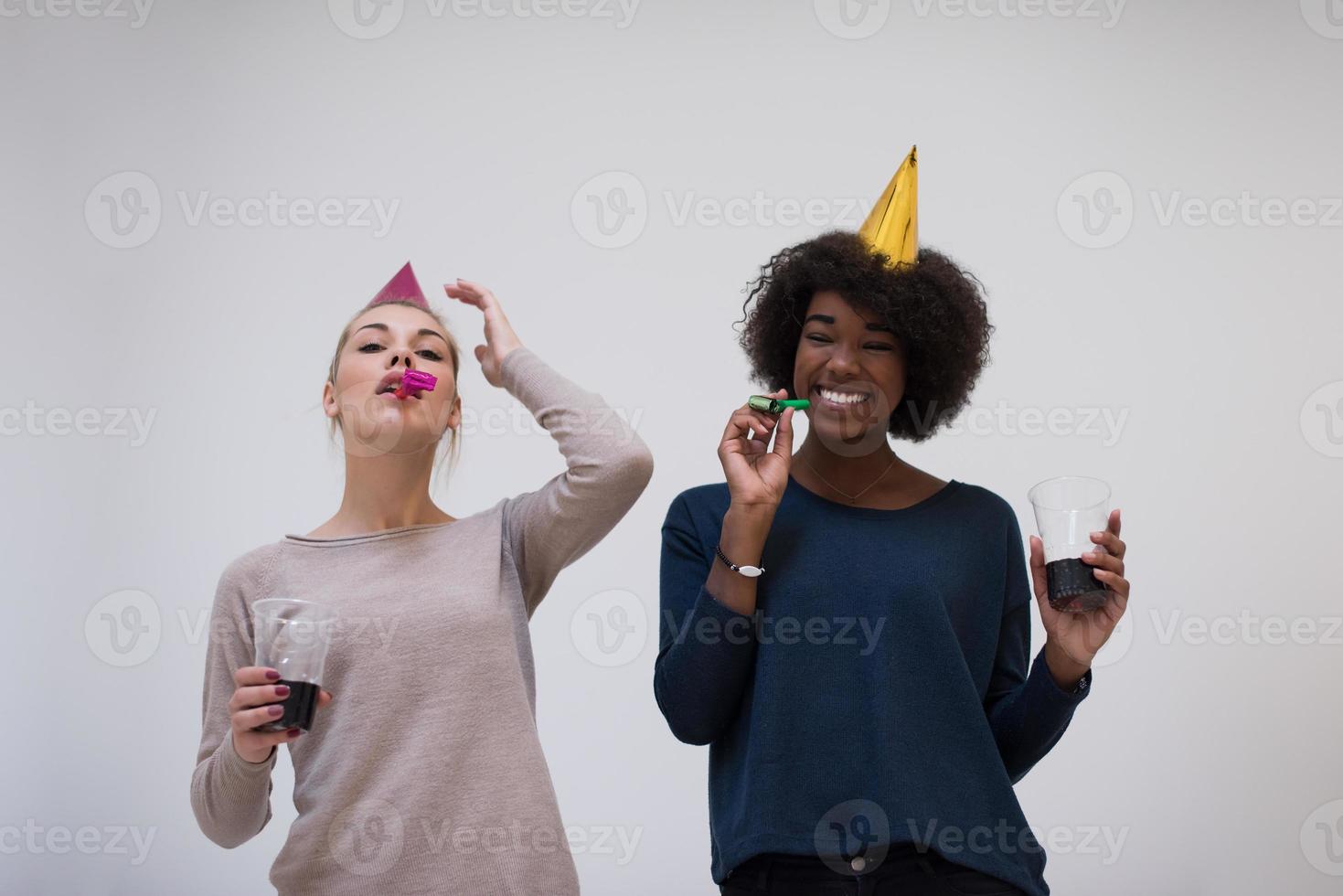 femmes souriantes en casquettes de fête soufflant aux sifflets photo