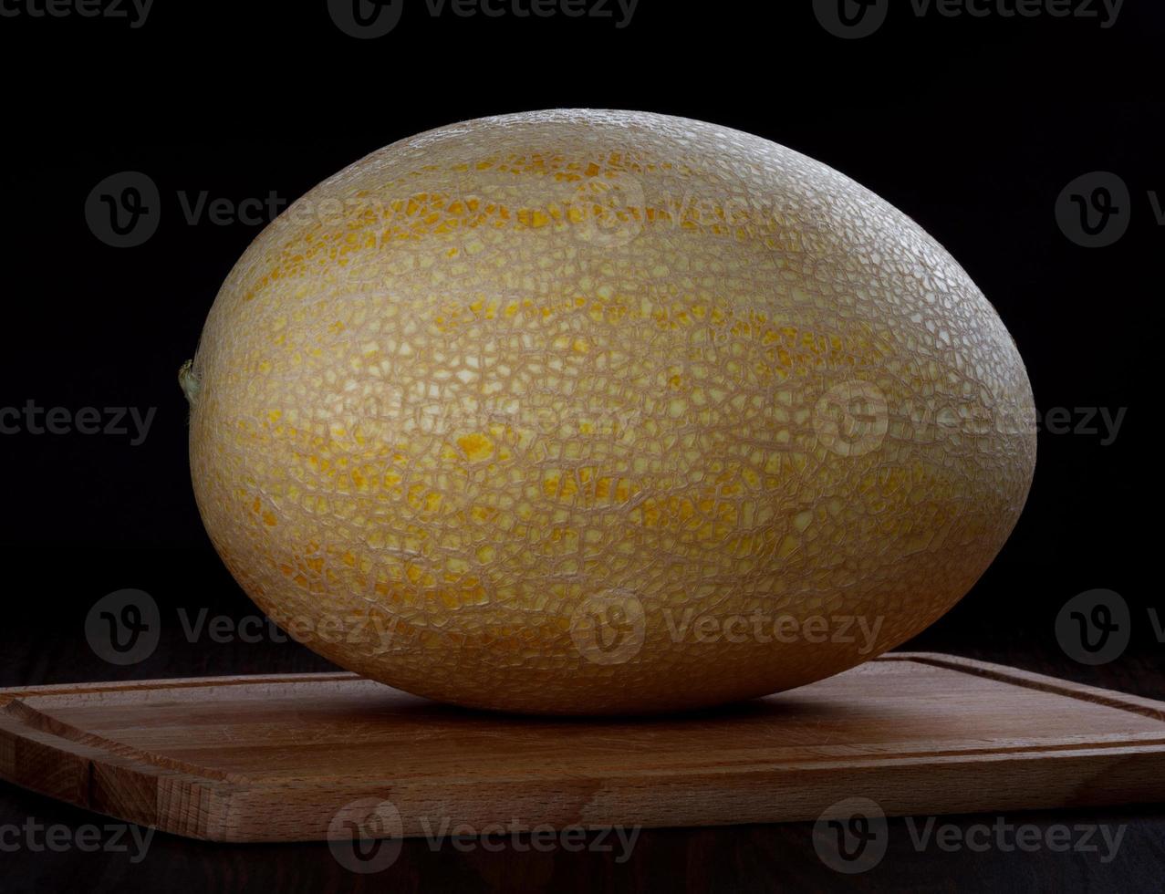 melon mûr jaune sur une planche à découper en bois sur fond noir. photo