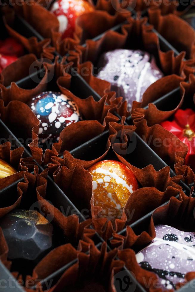 Chocolats artisanaux colorés dans une boîte sur fond sombre photo