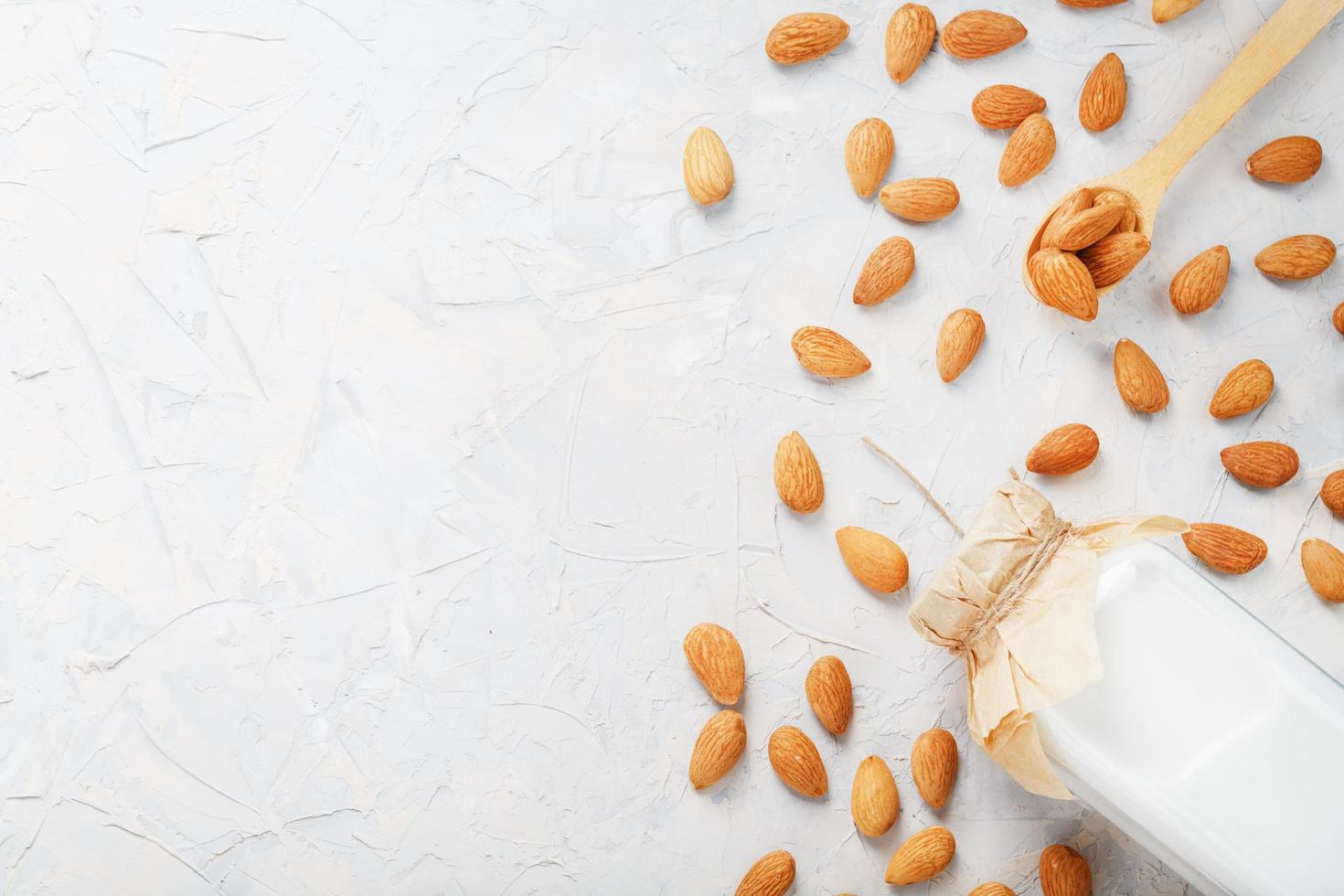 lait d'amandes biologiques dans une bouteille transparente avec une dispersion de graines et une cuillère en bois sur fond clair photo