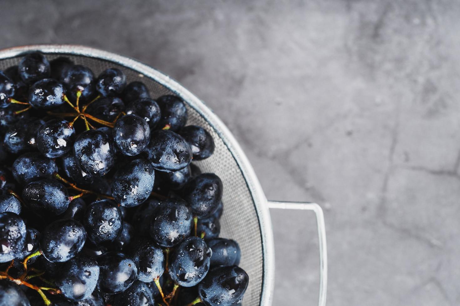 raisins noirs mûrs dans un bol en métal sur fond noir. photo