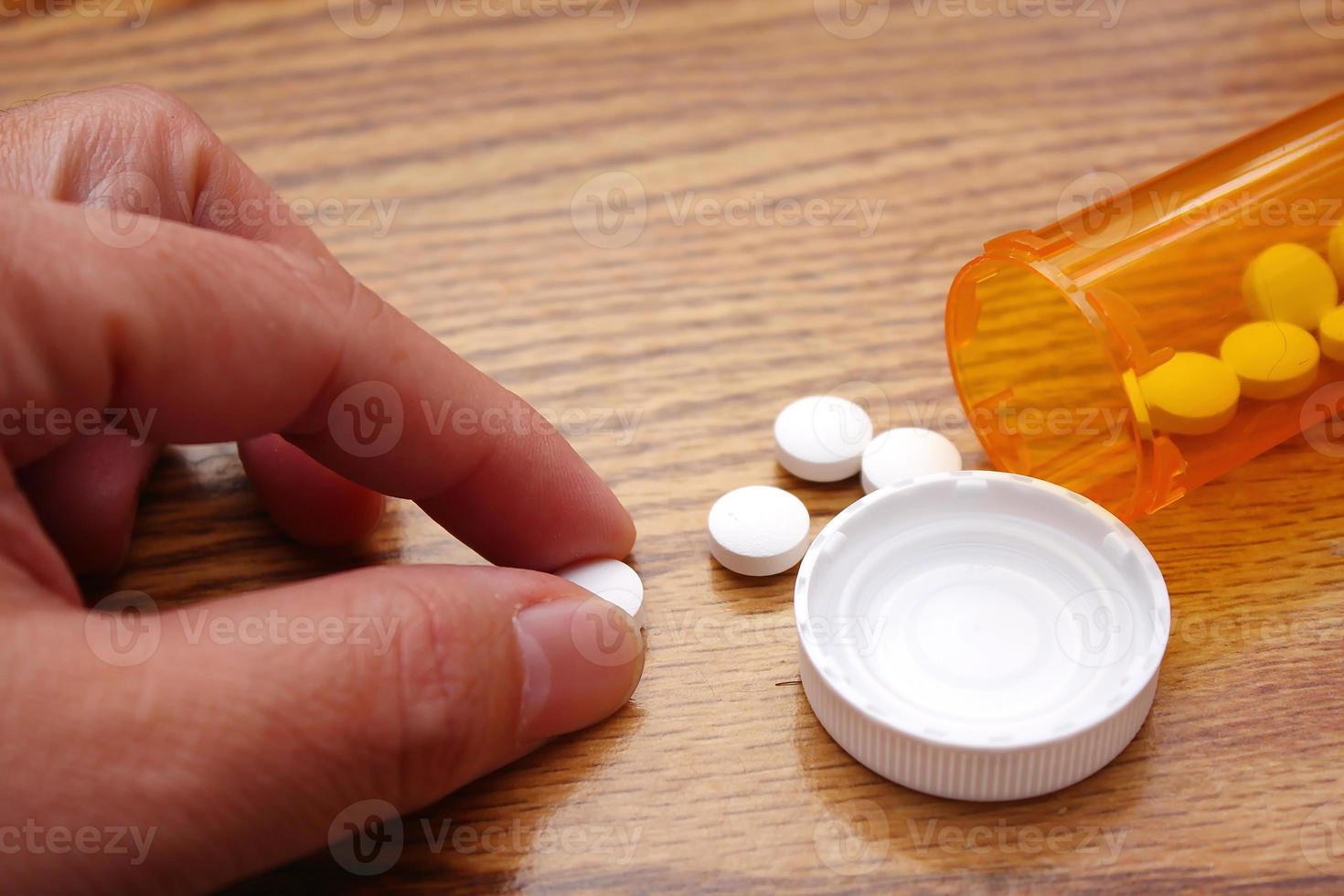 la main d'un homme prend des pilules d'une bouteille de pilules orange sur une table en bois, une pilule de médecine sur une table en bois. photo