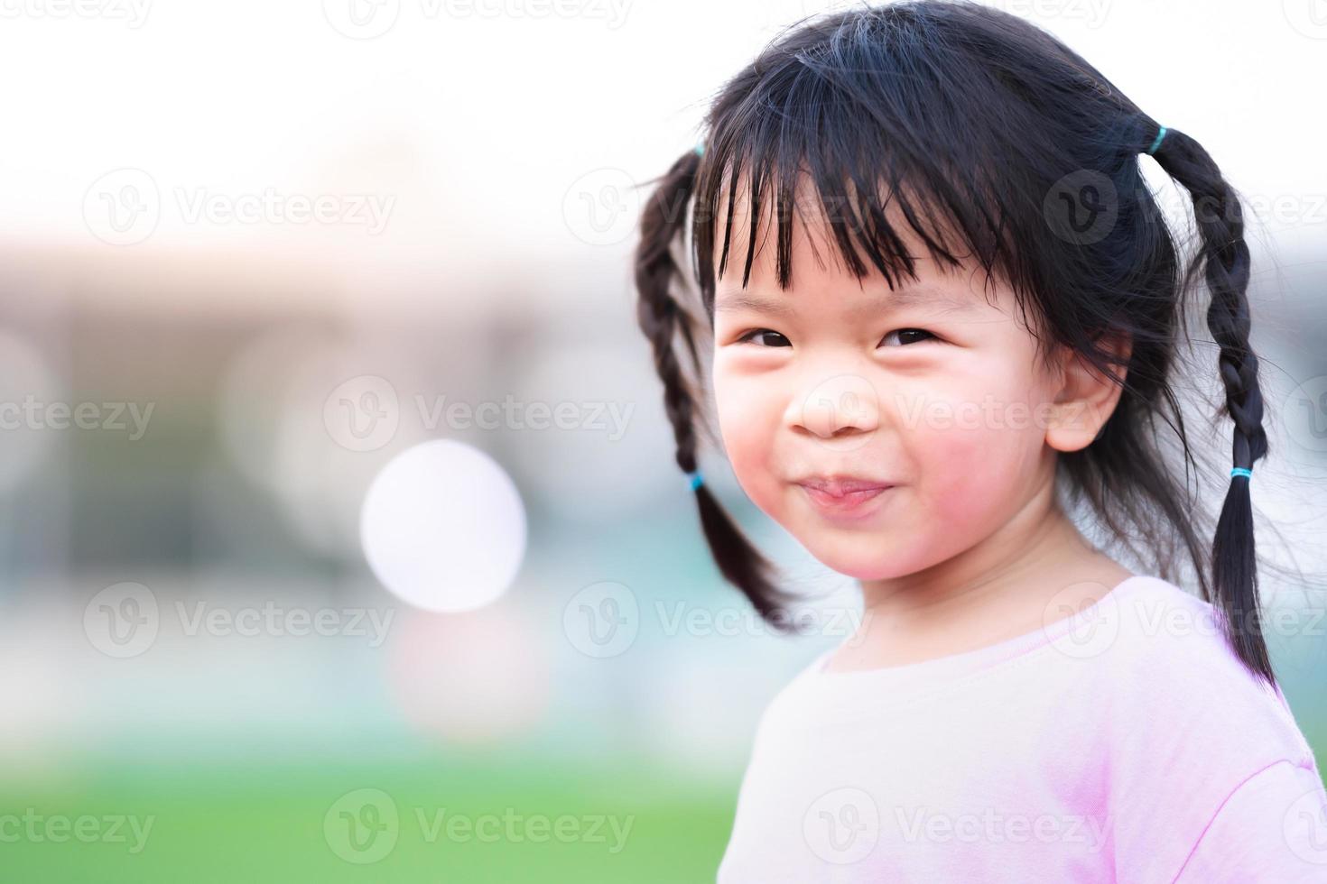 portrait de visage asiatique enfant fille doux sourire. enfant heureux avec un arrière-plan flou bokeh le soir. bébé mignon avec des cheveux noirs tressés deux tresses de chaque côté. espace de copie. photo