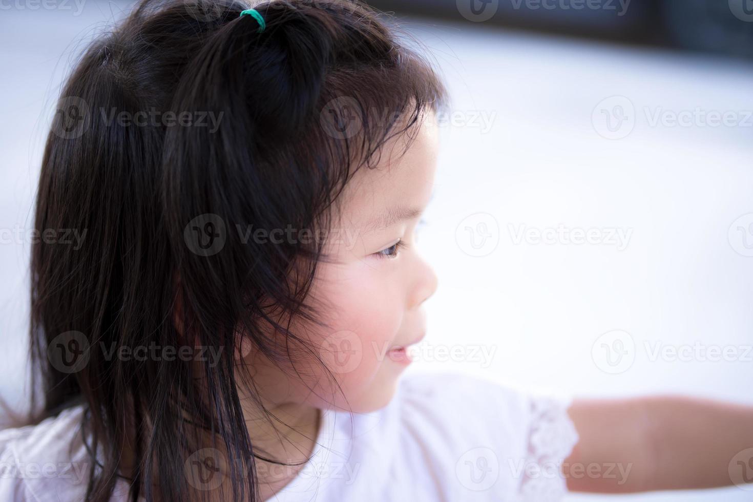 gros plan vue latérale petit sourire doux enfant mignon. candide fille asiatique heureuse. enfants âgés de 3 à 4 ans portant une chemise blanche. elle joue devant la maison. photo