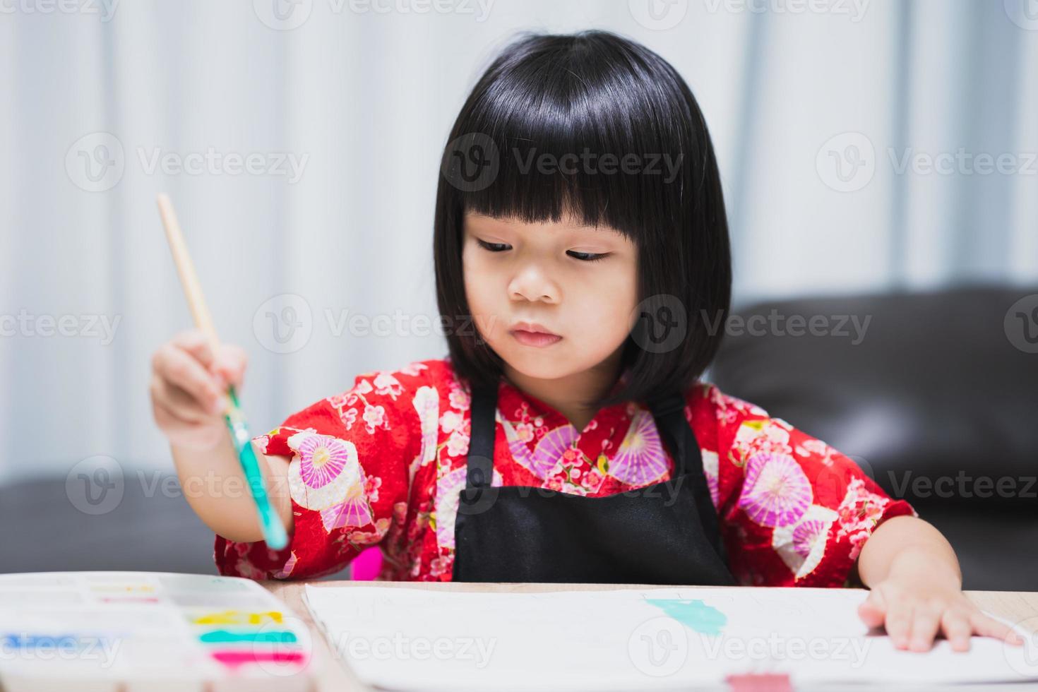 petite fille asiatique intelligente ayant une idée de faire de l'art comme passe-temps à la maison. apprentissage et éducation de l'enfant. enfant faisant de l'artisanat pour l'école à la maison dans la classe de cours. bébé de 4 à 5 ans porte une chemise rouge. photo