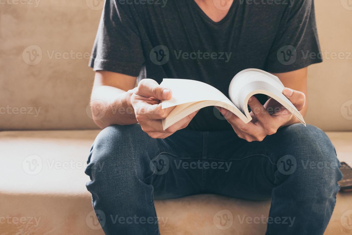 gros plan d'un jeune homme décontracté assis sur un canapé et lisant un livre à la maison. photo