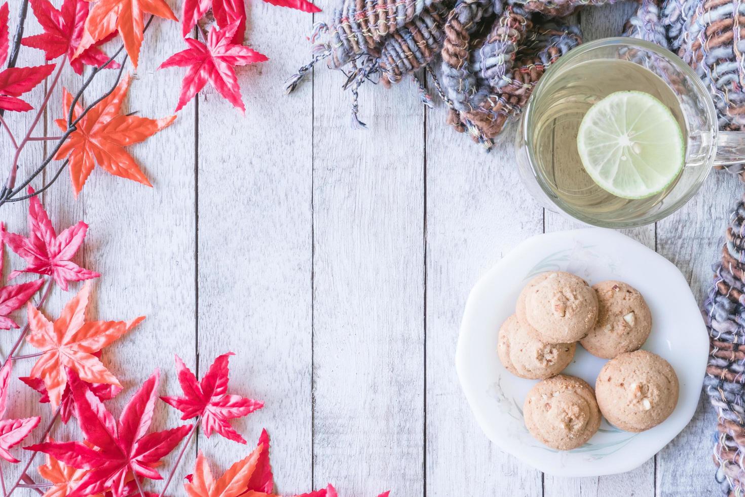 tasse de thé au citron, biscuit, écharpe et feuilles d'érable sur une table en bois peinte en blanc. photo