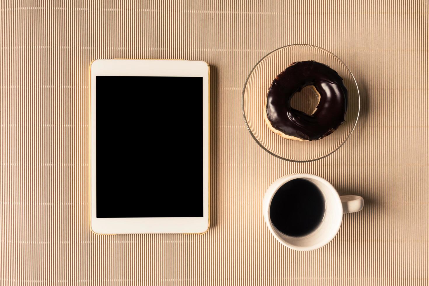 vue de dessus de la tablette avec une tasse de café et un beignet sur la table. photo