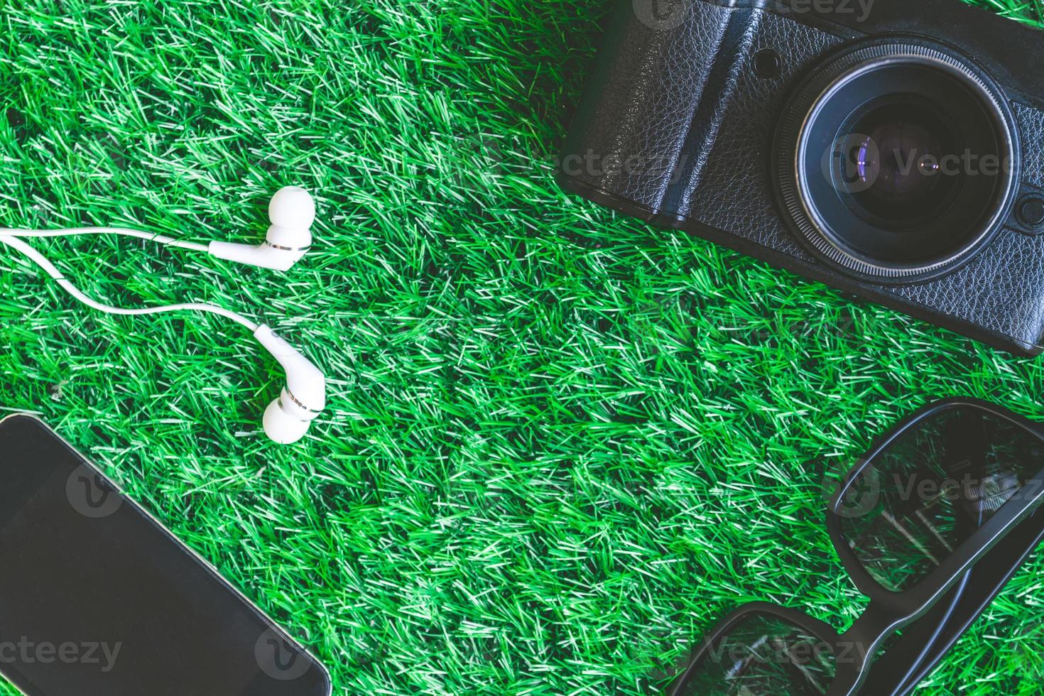 appareil photo avec lunettes de soleil, téléphone intelligent et écouteurs sur fond d'herbe verte.