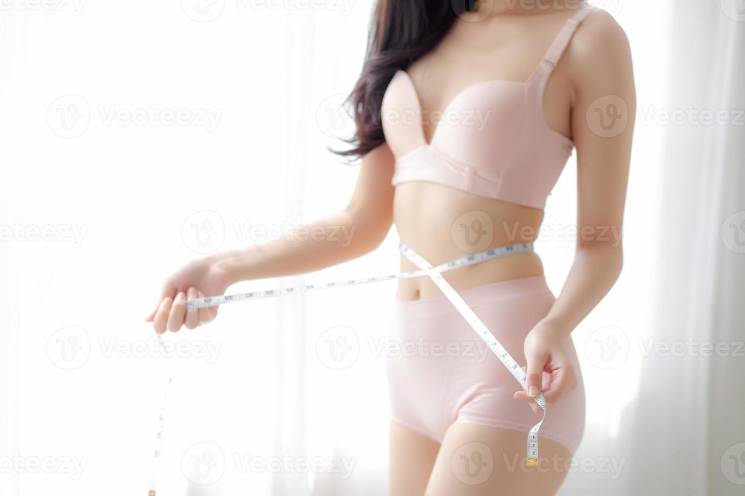 belle jeune femme asiatique corps sexy mince mesurant l'abdomen pour contrôler la perte de poids dans la chambre, belle fille ventre mince ont de la cellulite avec un ruban à mesurer pour le concept de régime, de santé et de bien-être. photo
