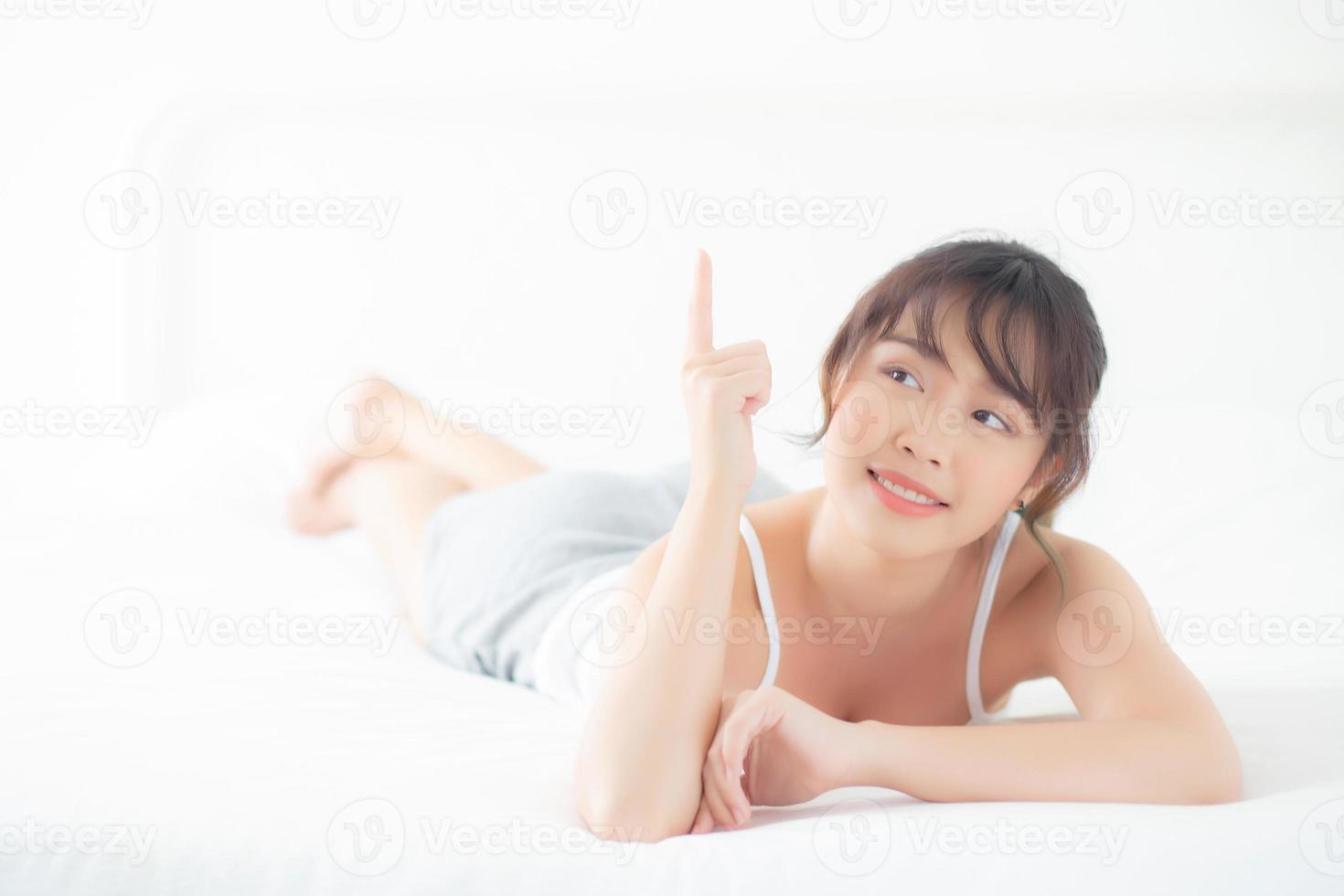 portrait belle jeune femme asiatique sourire réveillez-vous en bonne santé et bien-être le matin, beauté asie fille allongée et pointant quelque chose soins de la peau et maquillage cosmétique avec concept heureux, mode de vie et détente. photo