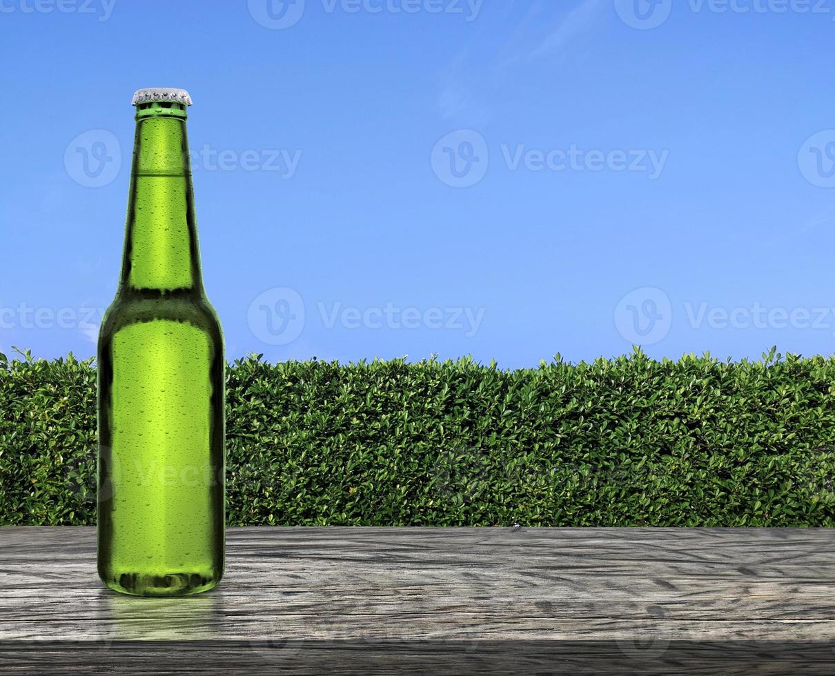 bouteille de bière avec des gouttes d'eau sur une terrasse de table en bois avec une texture de mur d'herbe verte et un ciel bleu vif photo