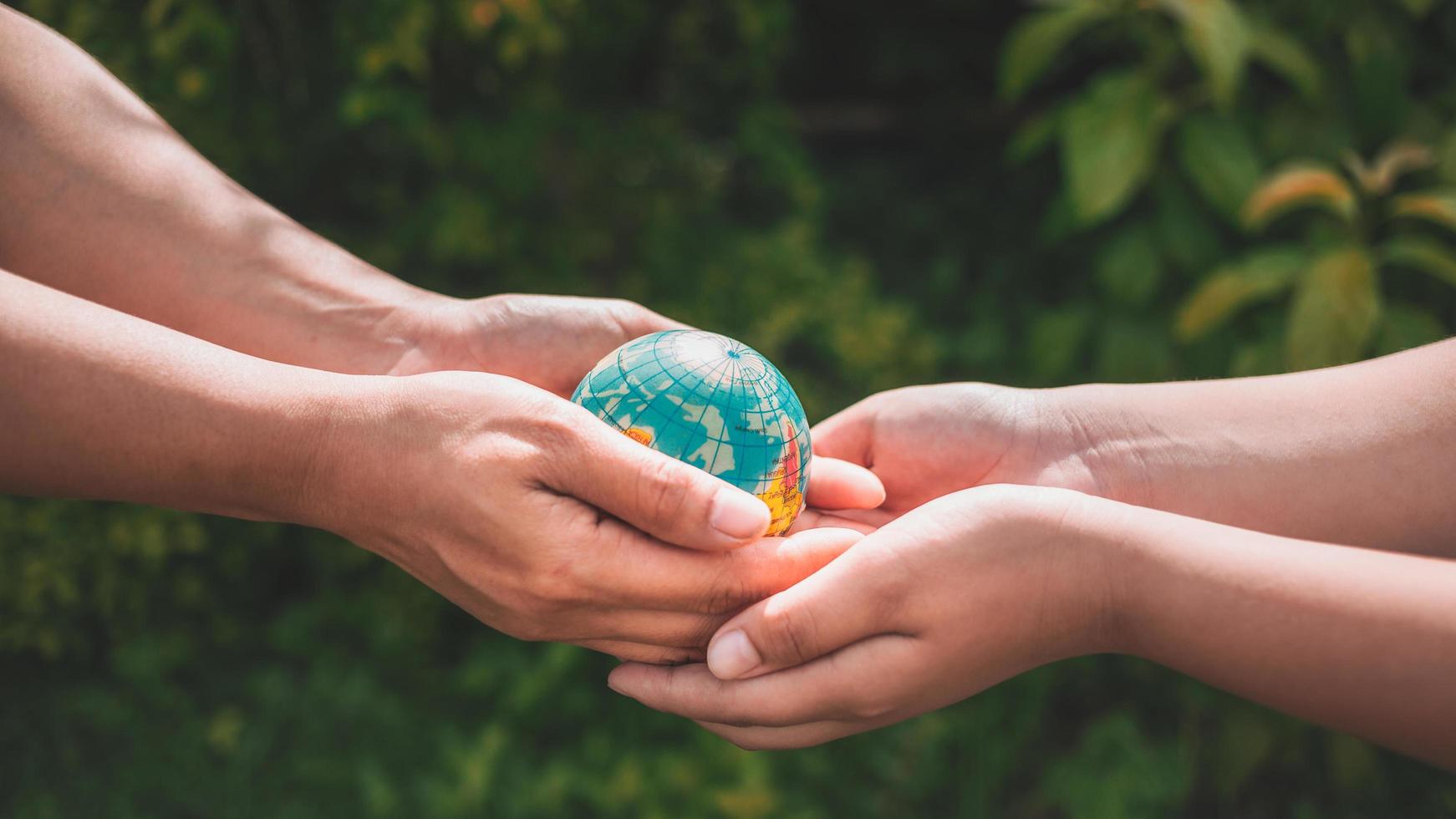 gros plan de la main d'une femme donnant un monde d'astéroïdes à un garçon sur un fond vert flou. les mains tenant la planète terre sauvent la terre. photo