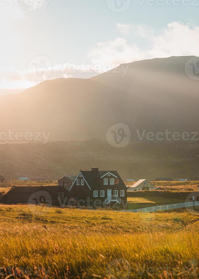 maison en bois islandaise qui brille de la lumière du soleil sur le pré et les oiseaux qui volent au coucher du soleil l'été au village de pêcheurs d'arnarstapi, islande photo