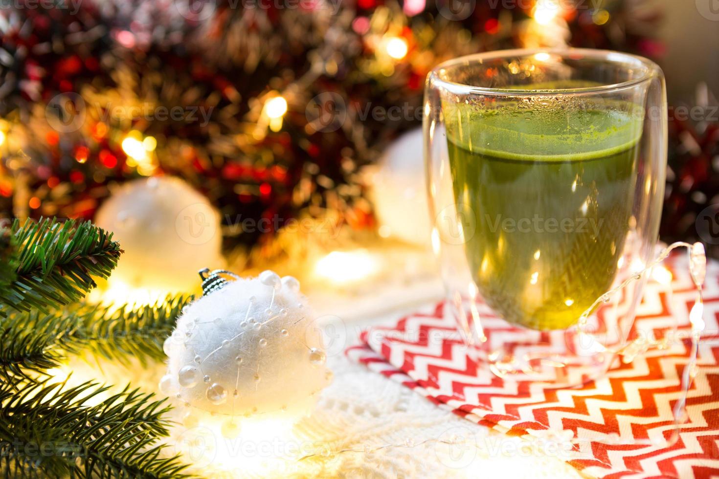 gobelet en verre transparent à double paroi avec thé matcha japonais sur table avec décor de noël. ambiance de nouvel an, guirlande et guirlande, branche d'épicéa, confortable, couverture tricotée, ballon, serviette rayée photo