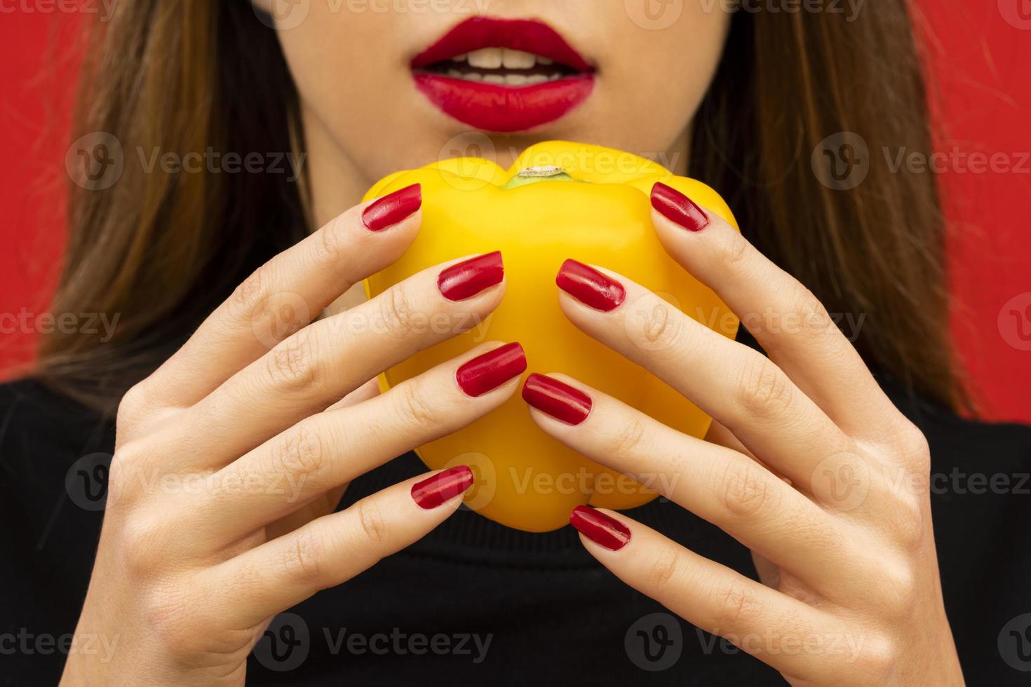 portrait de belle jeune femme tenant un poivron jaune sur fond rouge photo