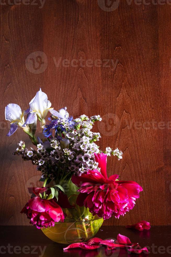 Diverses fleurs dans un vase sur fond marron foncé photo