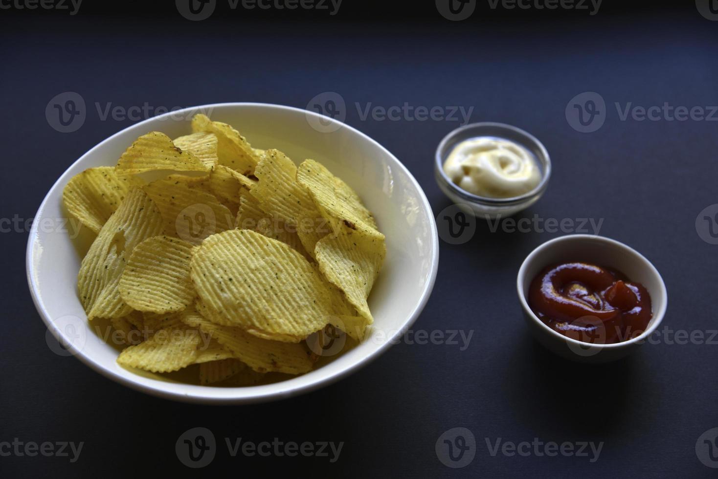délicieuses chips de pommes de terre avec des sauces sur fond noir. apéritif de croustilles avec sauce. restauration rapide sur fond noir. photo