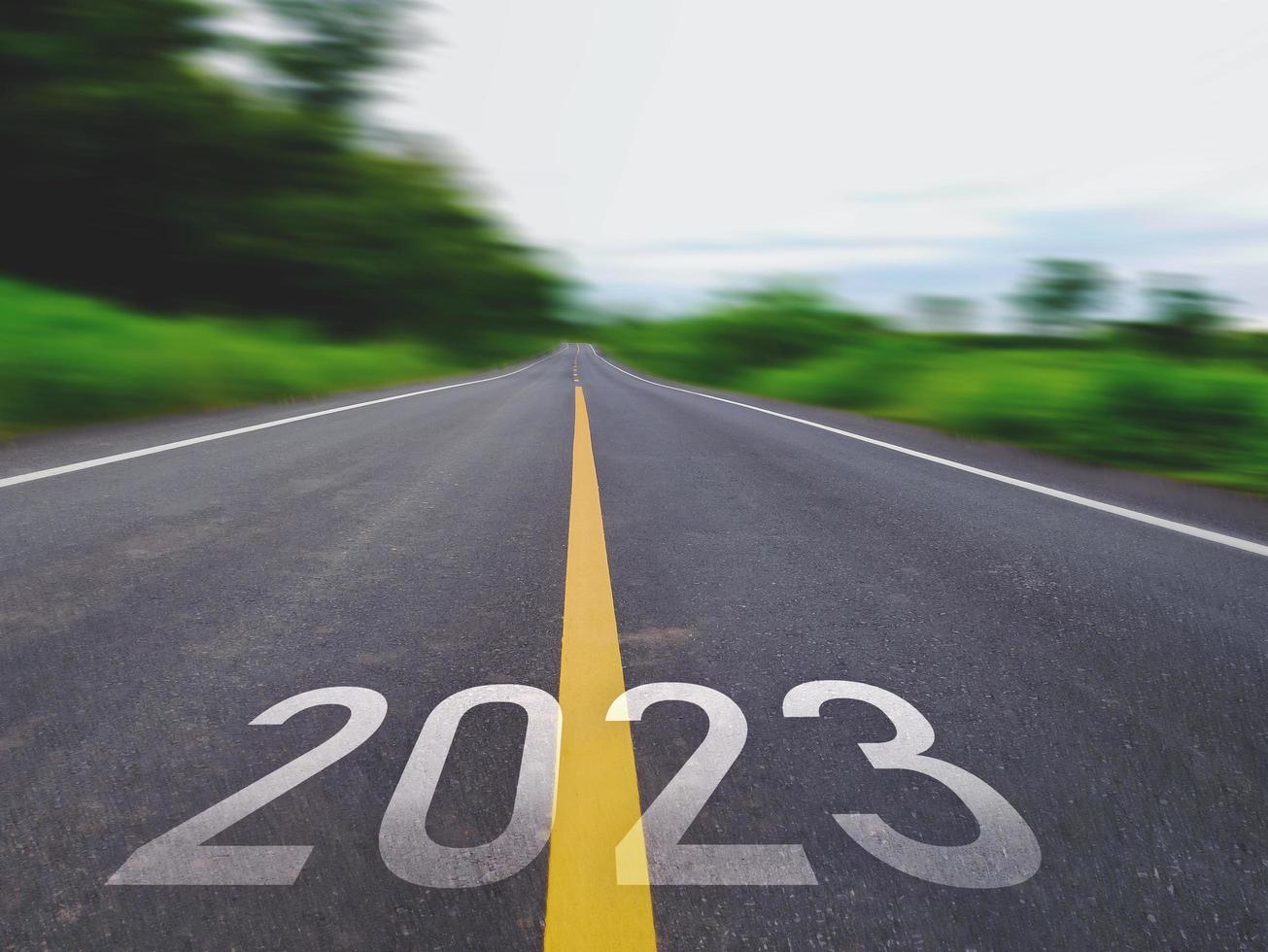 concept de nouvelle année et nouvelle route avec le mot 2022 à 2023 écrit sur la route goudronnée dans une belle route de campagne avec des champs d'herbe verte des deux côtés concept pour la nouvelle année ou vision de 2023 photo