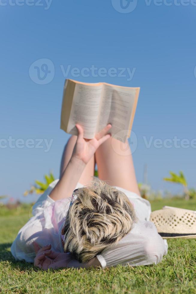 femme allongée et lisant son livre préféré sur un pré recouvert d'herbe verte fraîche par un été ensoleillé ou une journée de printemps. photo