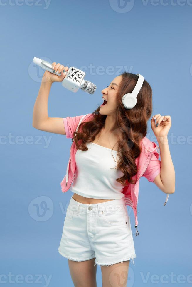 belle fille asiatique avec microphone chante et casque isolé sur fond bleu. photo