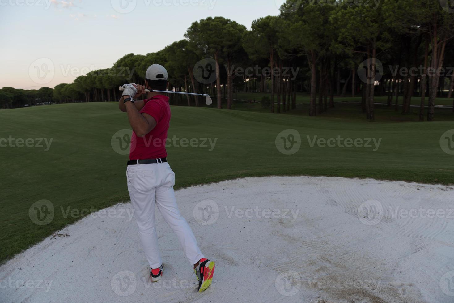 golfeur frappant un bunker de sable tourné au coucher du soleil photo