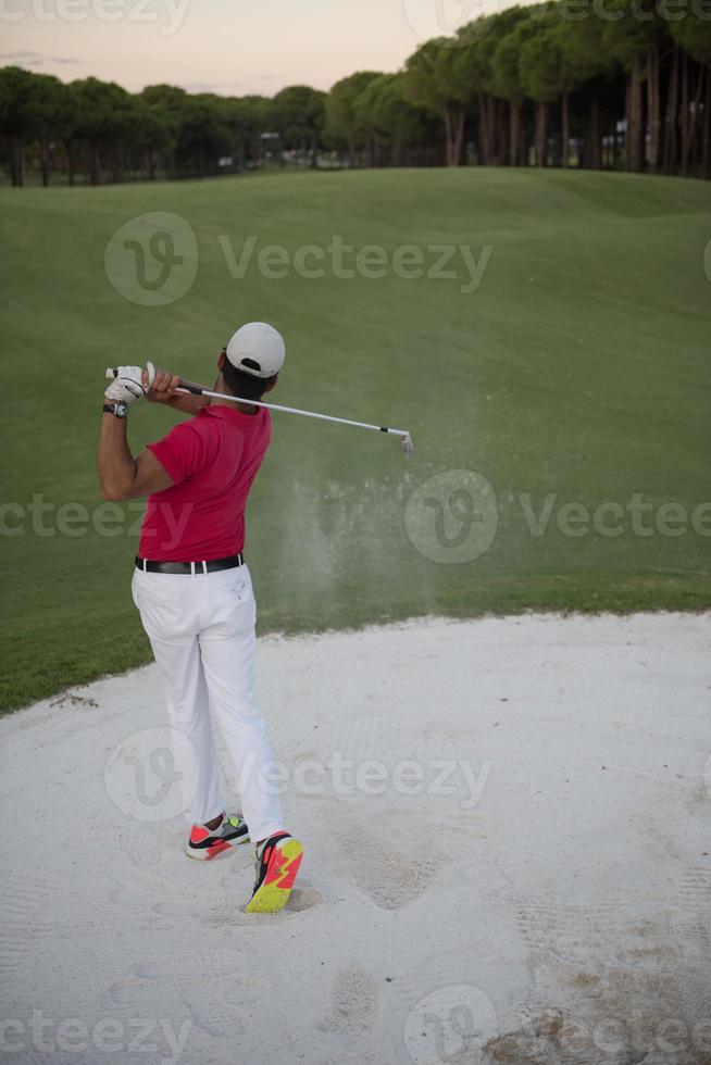 golfeur frappant un bunker de sable tourné au coucher du soleil photo