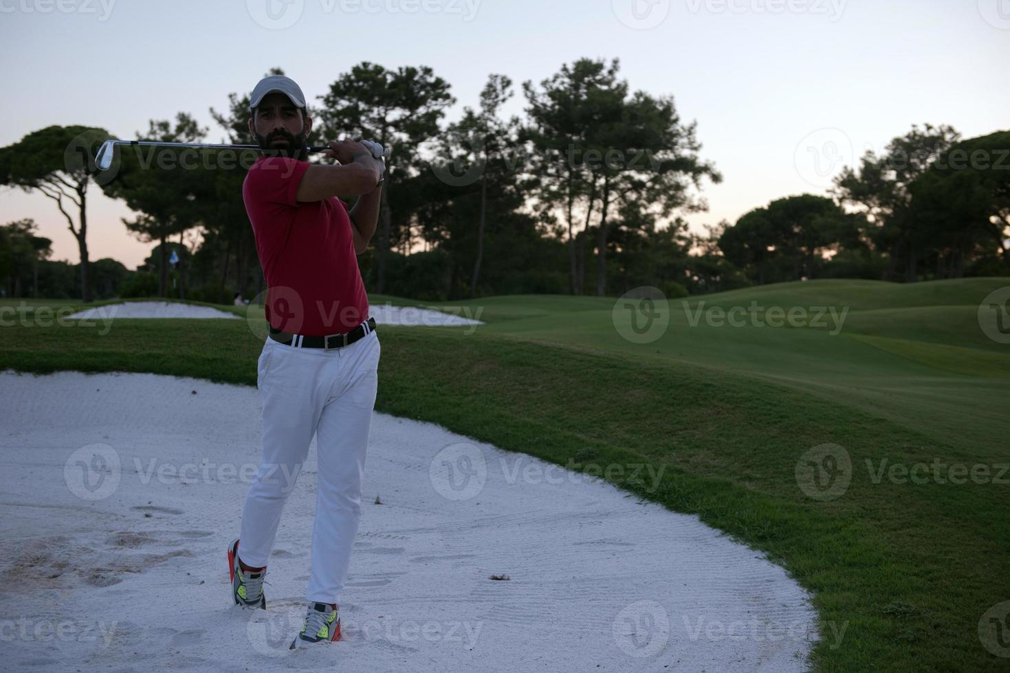 golfeur frappant un bunker de sable tourné au coucher du soleil photo