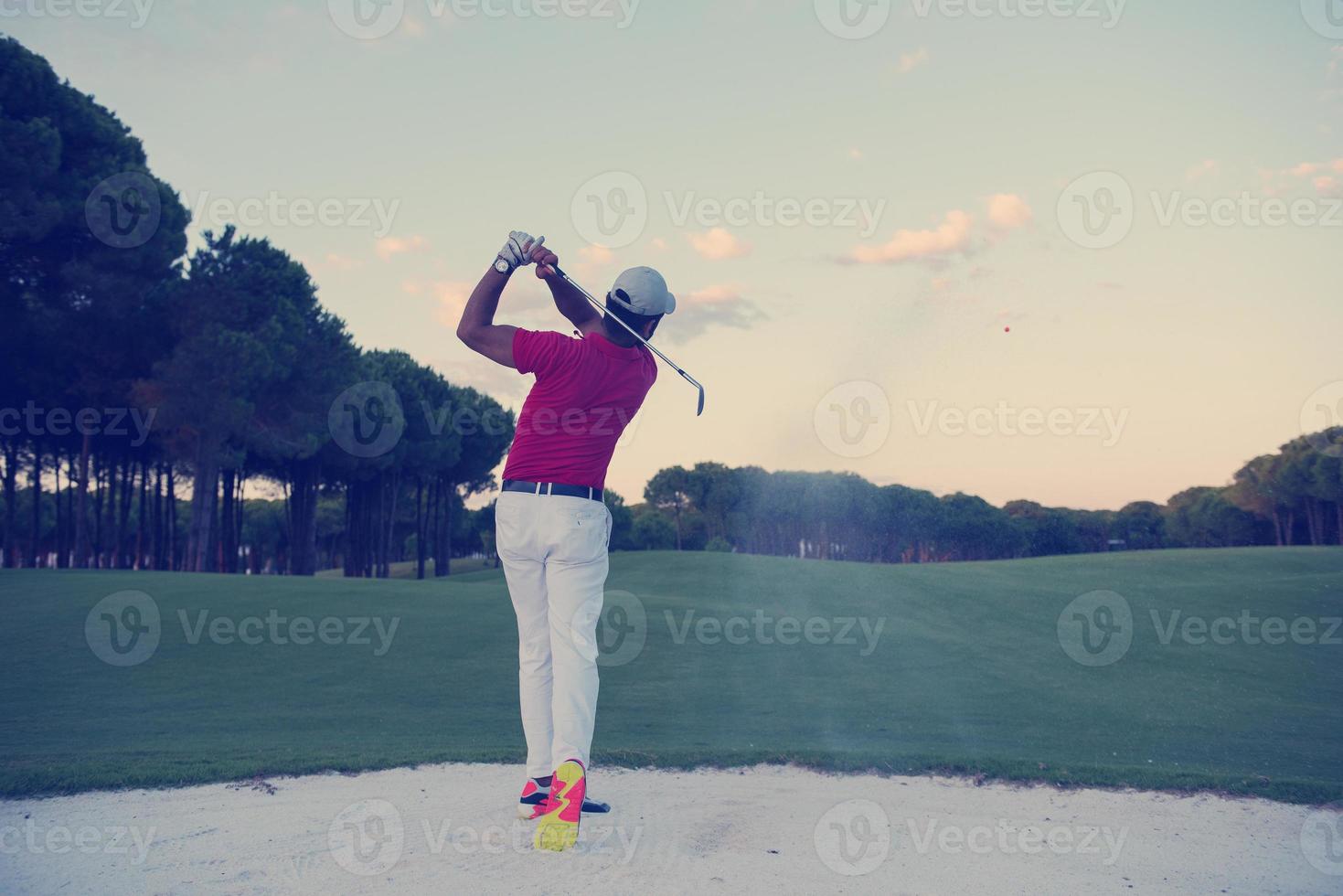 golfeur frappant un bunker de sable tourné au coucher du soleil photo