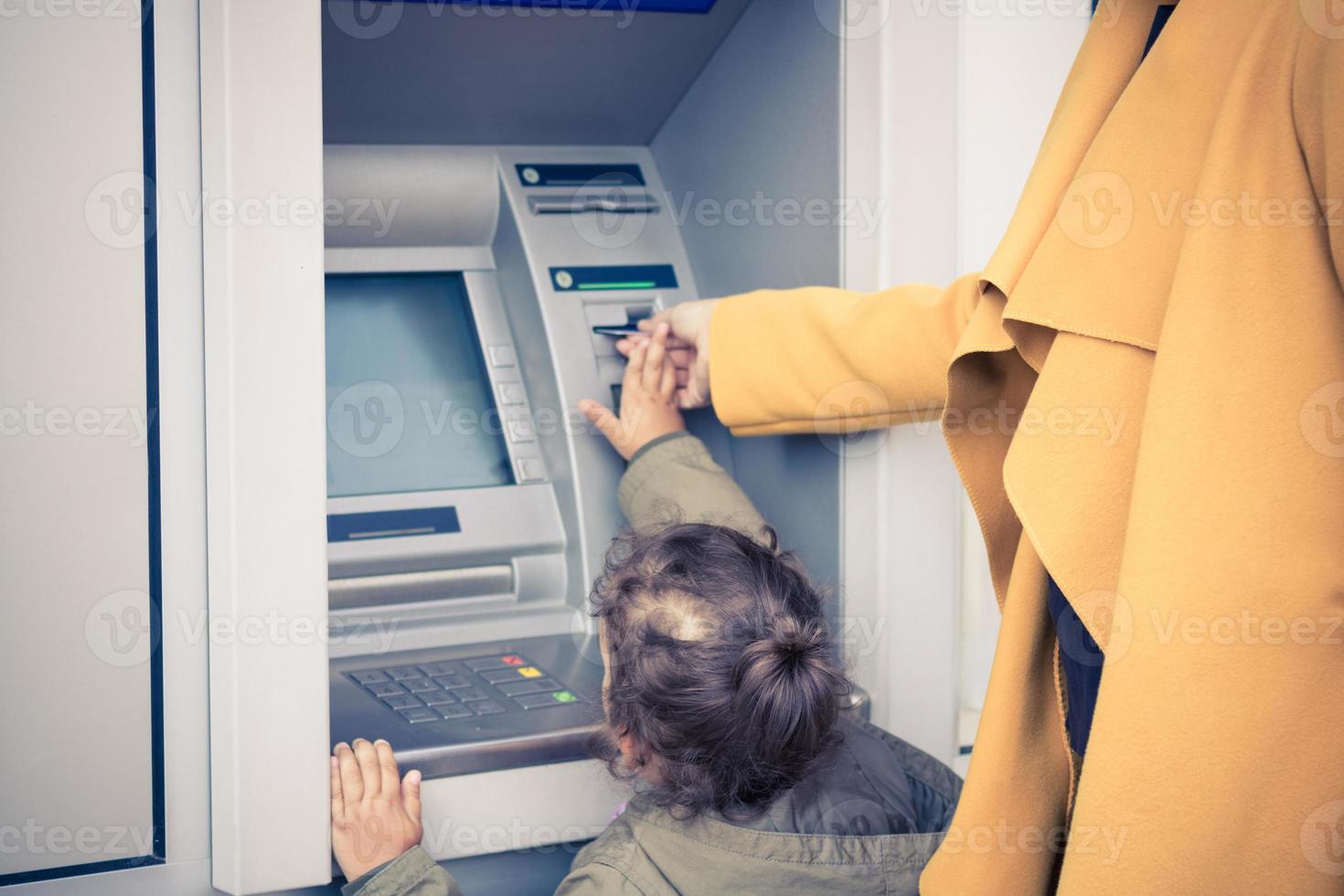 petite fille retirant de l'argent sous forme d'atm avec l'aide de sa mère. photo