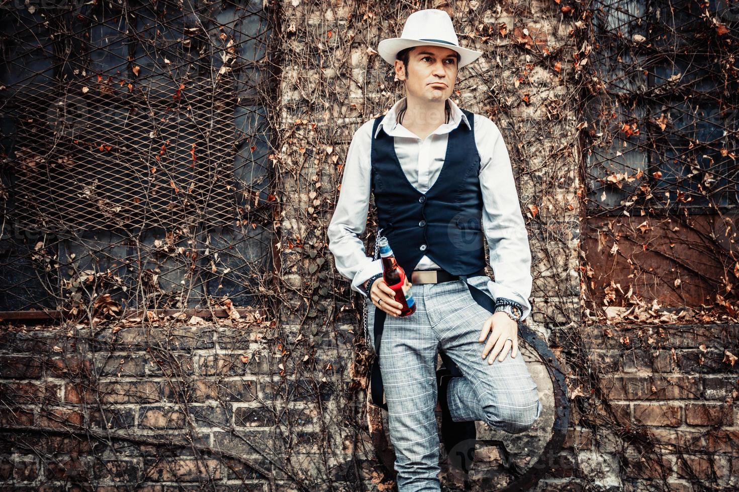 homme pensif avec une bouteille de bière appuyée sur un mur et regardant ailleurs. photo