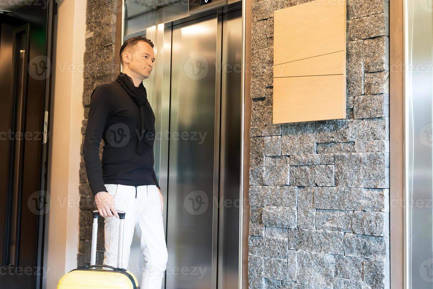 homme adulte moyen avec valise en attente de l'ascenseur. photo