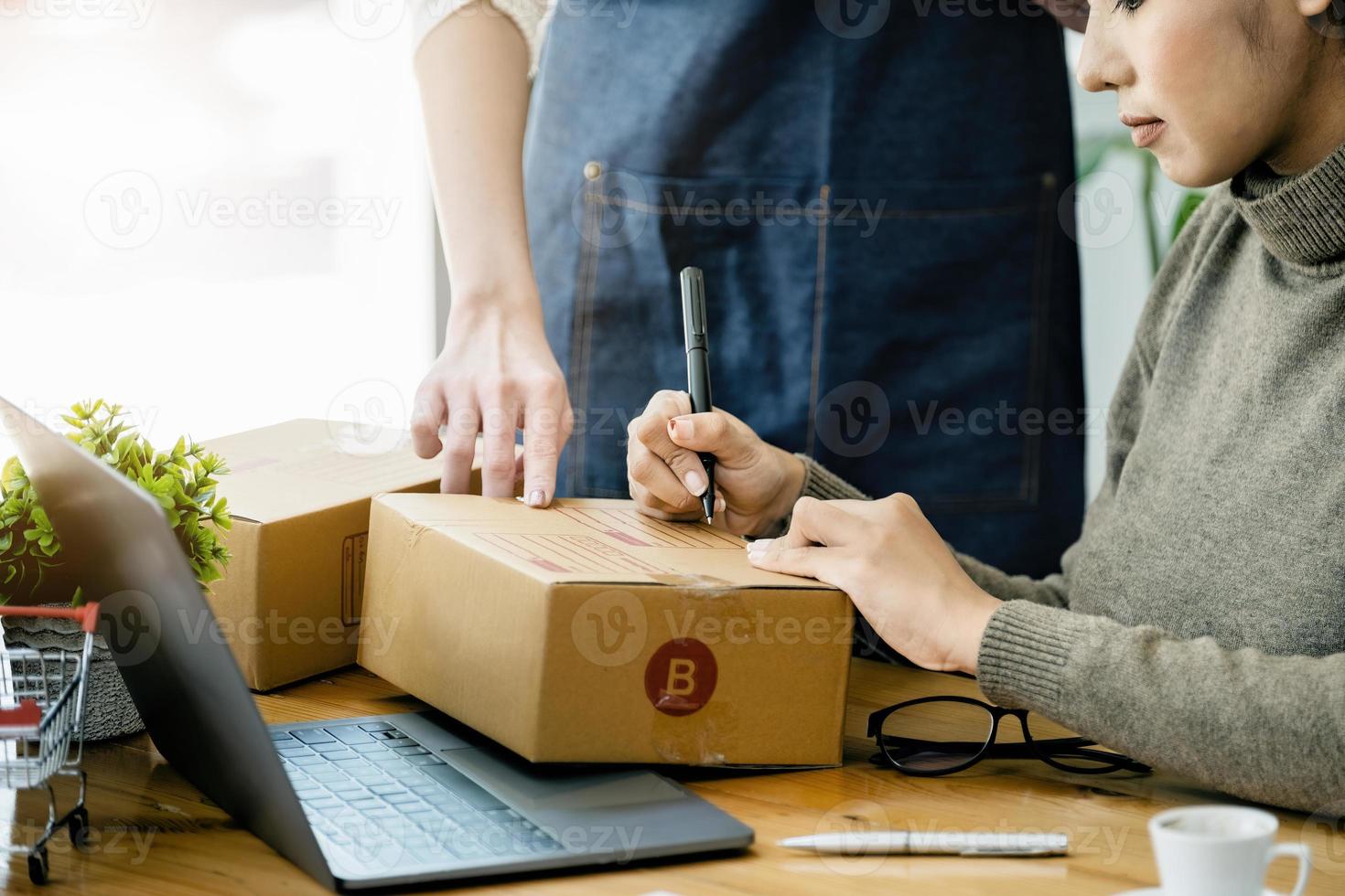 deux femmes heureuses vendant des produits en ligne. démarrer un propriétaire de petite entreprise avec un stylo pour écrire les adresses des clients et les préparer pour l'affranchissement. photo