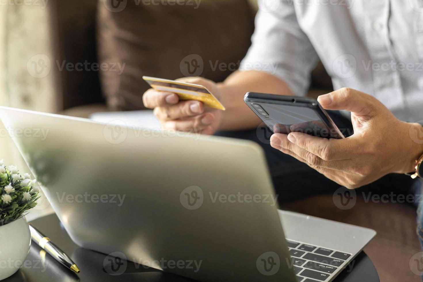 homme tenant une carte de crédit et utilisant un smartphone à la maison, homme d'affaires faisant des achats en ligne, commerce électronique, services bancaires par Internet, dépenser de l'argent, travailler à domicile, s'asseoir sur le canapé dans le salon à la maison. photo